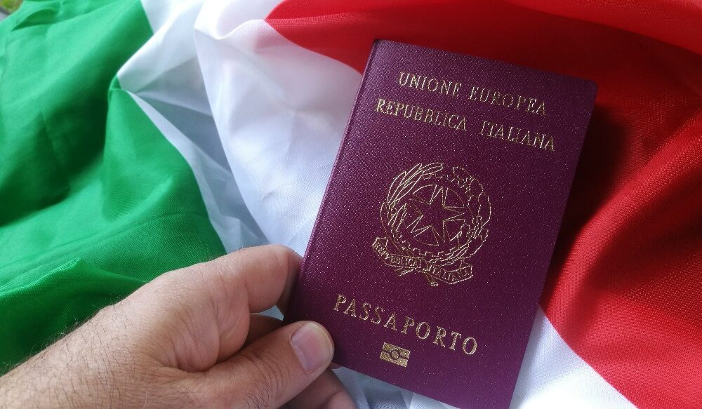 A vibrant shot of a burgundy Spanish biometric passport with the "Plus Ultra" coat of arms, resting on a smartphone showing a "Cita Confirmada" (Appointment Confirmed) screen.